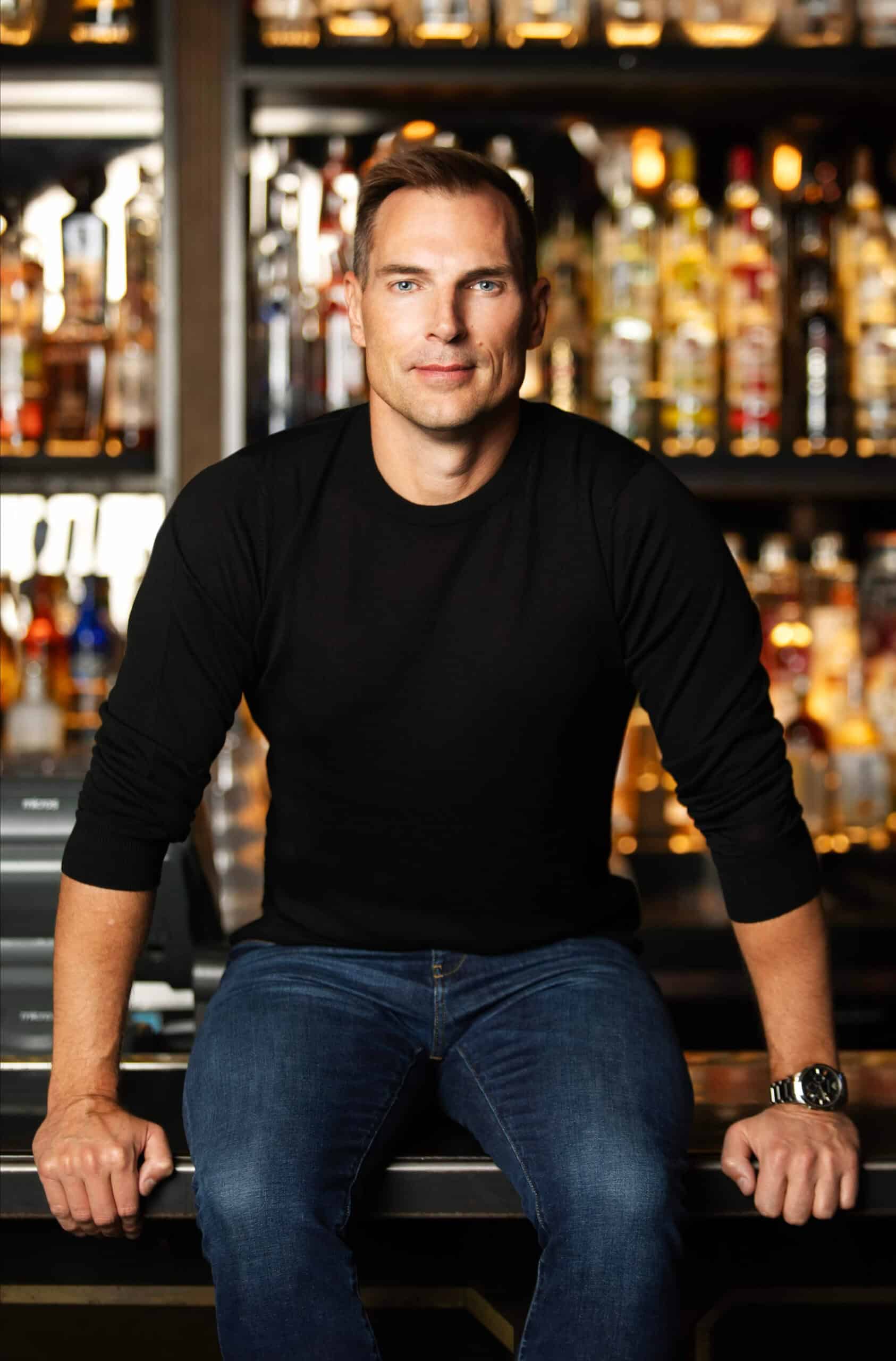 Bartender at a bar with a variety of liquor bottles in the background.